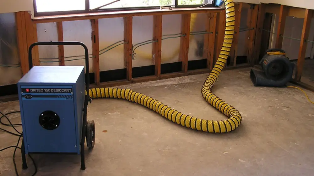 Dehumidifier with a yellow duct drying a room with wall panels removed