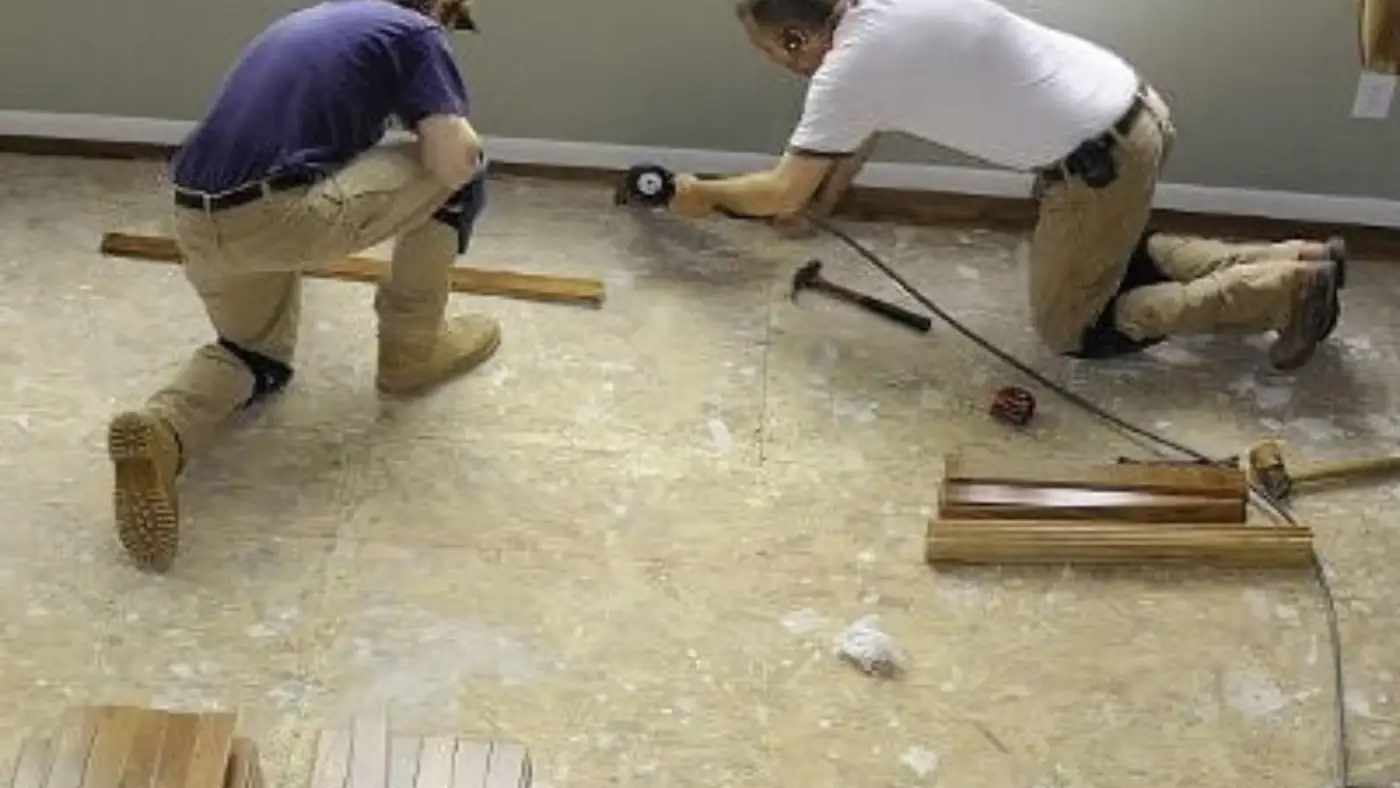 Two workers kneeling on a subfloor to repair flooring after a leak